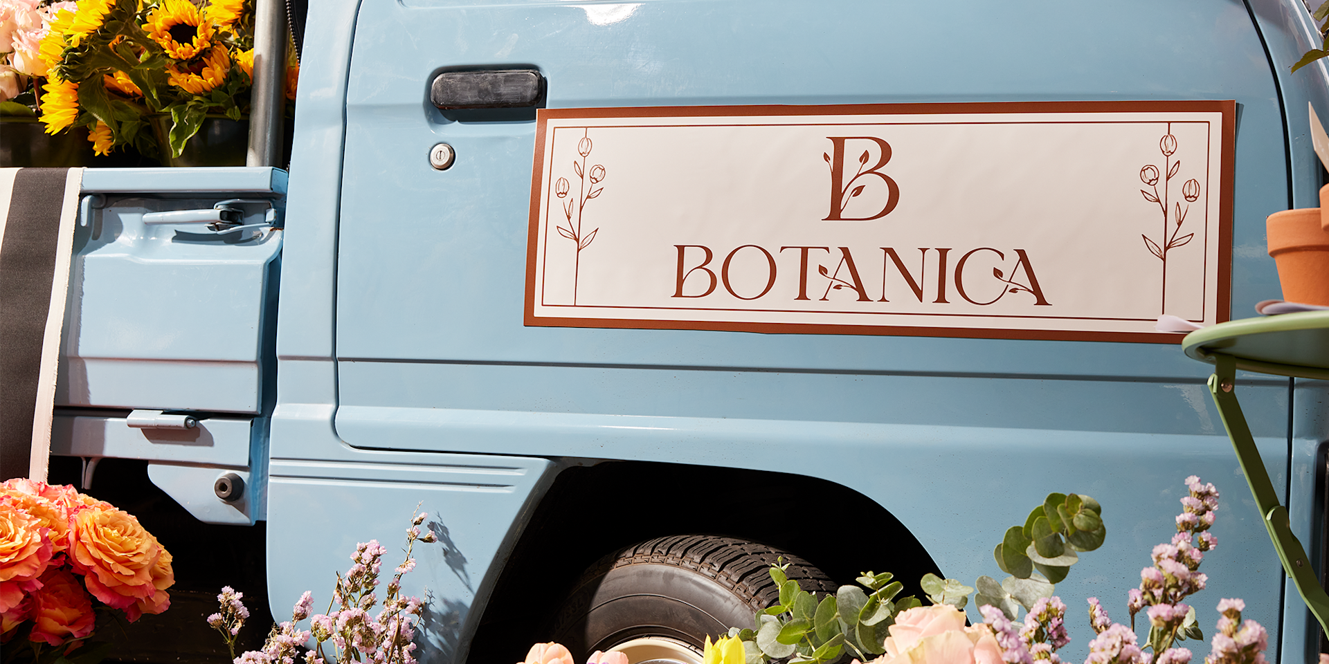 A truck featuring a car magnet for a florist, with a flower delivery and plants in the background.