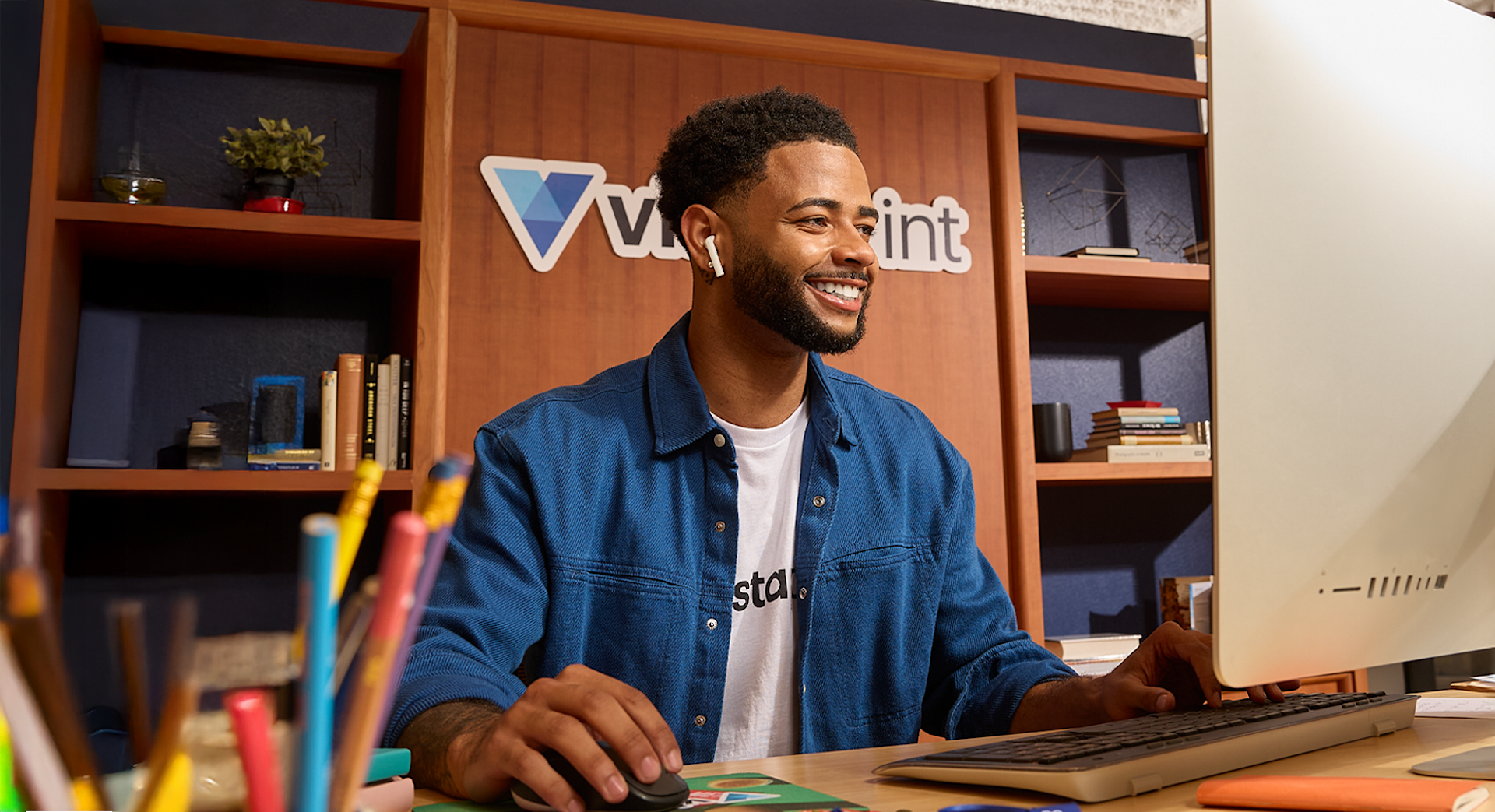 A support specialist at a desk smiling while helping customers online.