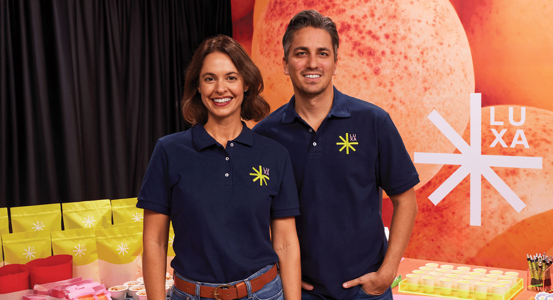 Two people in navy custom polo shirts with an embroidered logo, standing at a colorful booth.