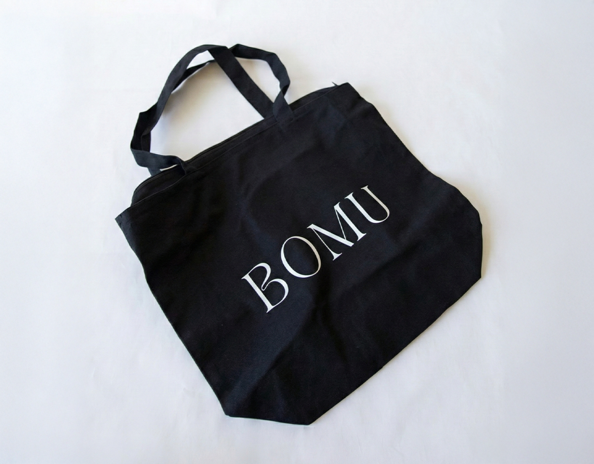 The tote bag is laid flat, clearly displaying its shape, size and overall design featuring the business name “Bomu”