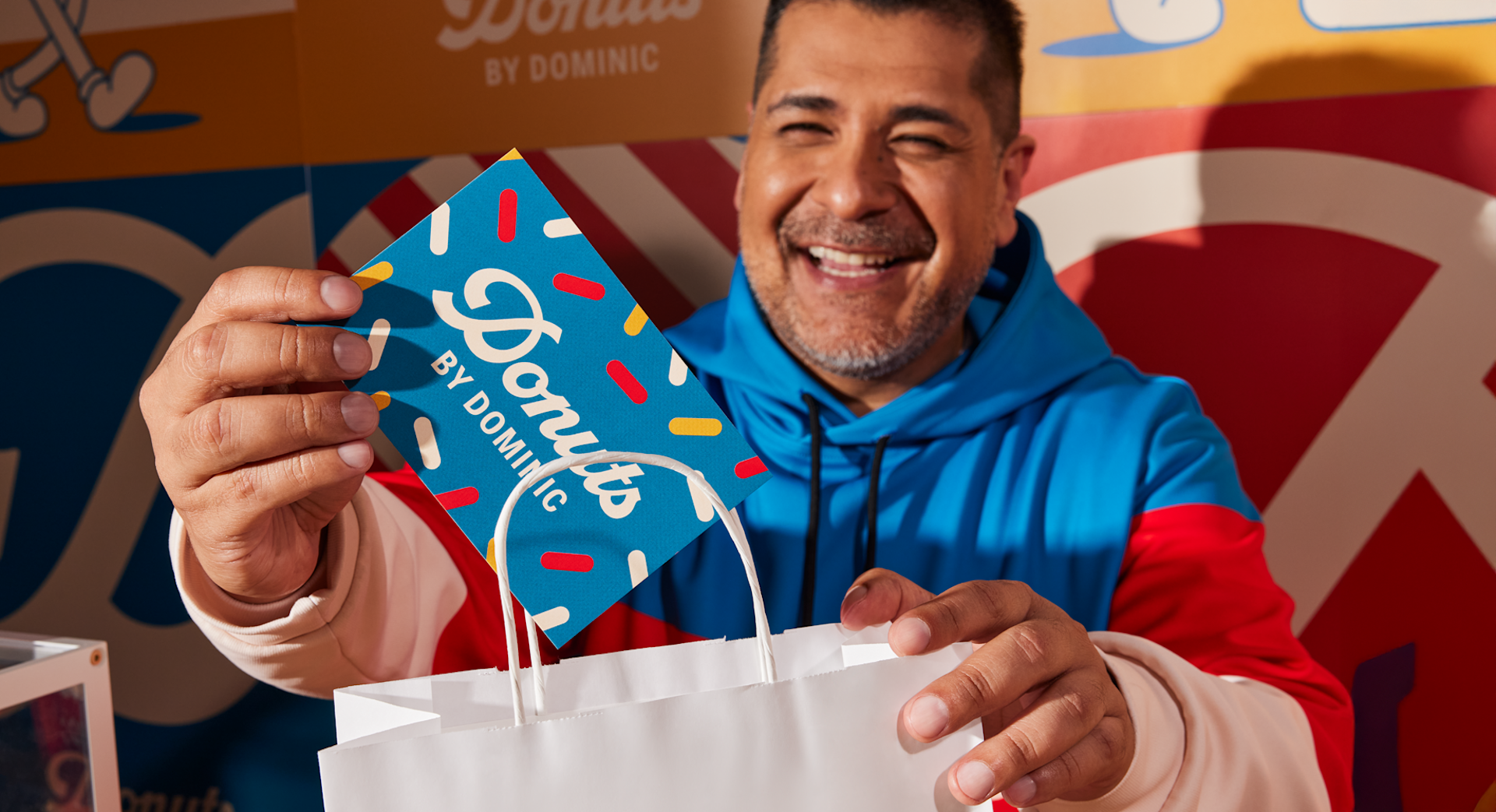 Un propietario de una venta de donas colocando una postal en una bolsa de comida para llevar.