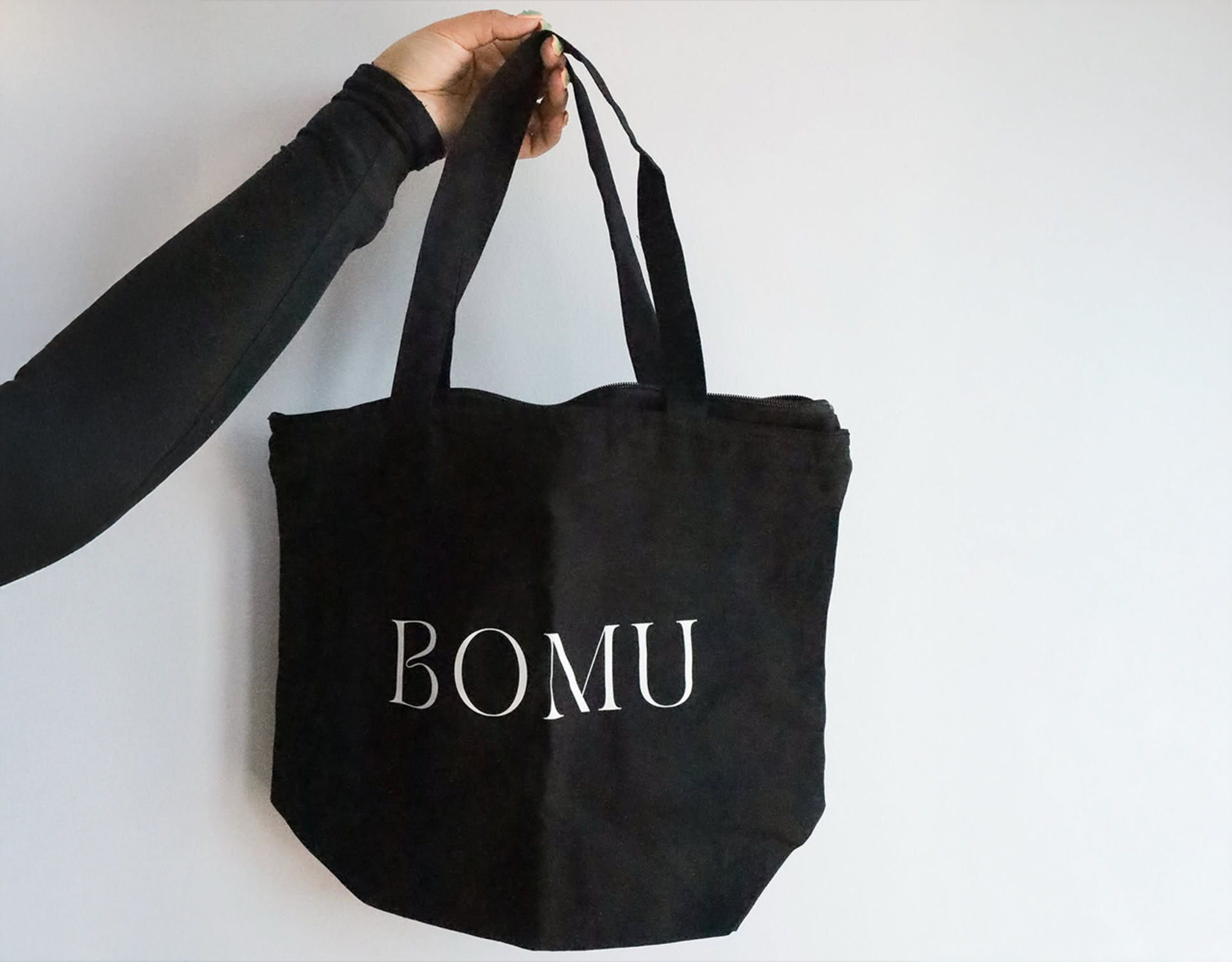 Una bolsa de tela negra con el nombre comercial «BOMU». La bolsa se sostiene por el asa, mostrando cómo luce cuando se carga. 