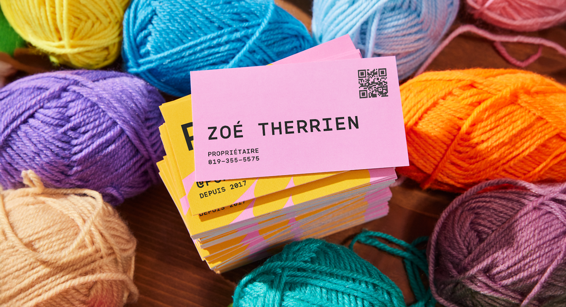 Un lot de cartes d’affaires avec code QR posé sur une pile de pelotes de laine colorées.