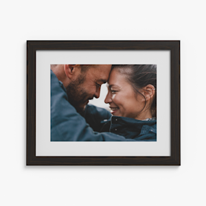 A framed print with a white border featuring a couple smiling. 