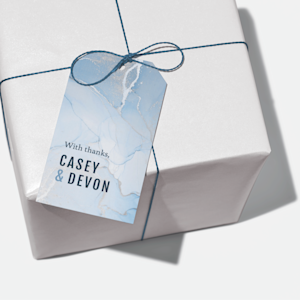 A plastic hang tag with a “thank you” message on it placed on a gift with blue ribbon.