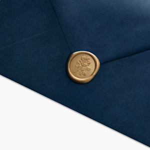 A navy envelope sealed with a gold-colored wax seal embellished with a floral design. 