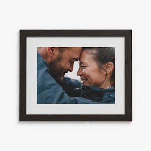 A black framed print with a white border, featuring a photo of a couple hugging.