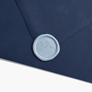 A navy envelope sealed with a gold-colored wax seal embellished with a floral design. 
