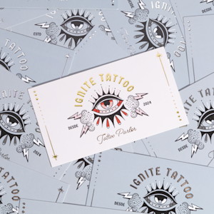 Una tarjeta de presentación con relieves metalizados promocionando un estudio de tatuajes.