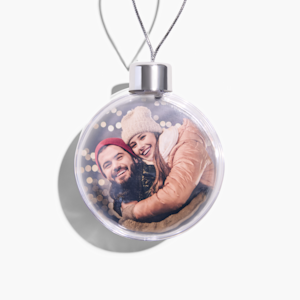 Een kerstbal met foto, voorzien van een foto van een jong stel dat elkaar omhelst. 