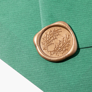 Een groene envelop, verzegeld met een lichtblauw waxzegel met bloemmotief.