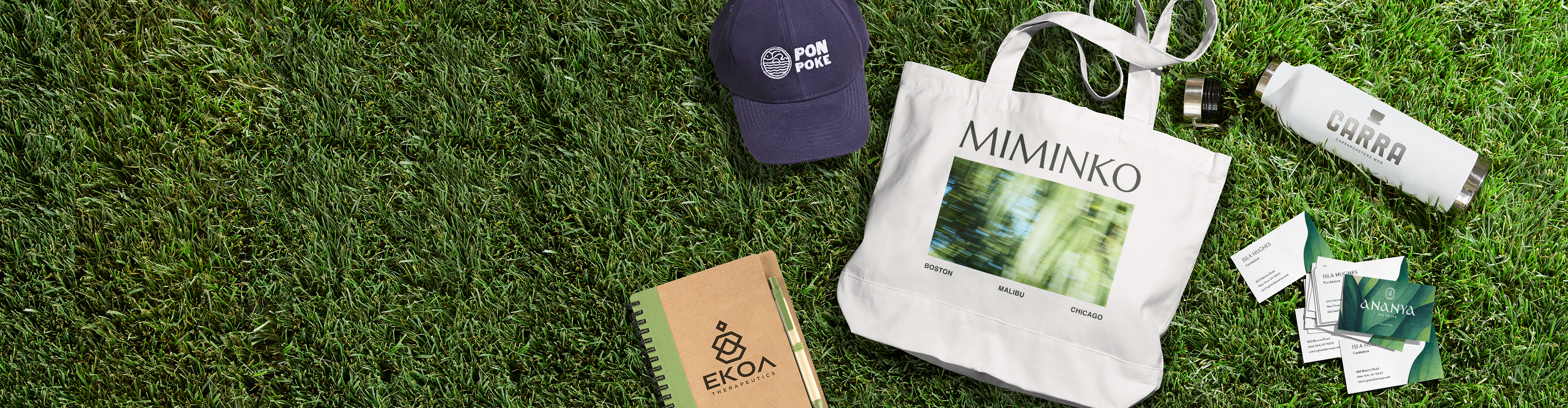 Better by Design branded merchandise on grass, including a tote bag, cap, notebook and other essentials.