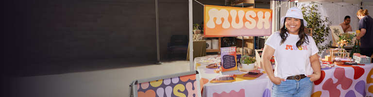 A business owner stands in front of a table showing off branded marketing and merchandise.
