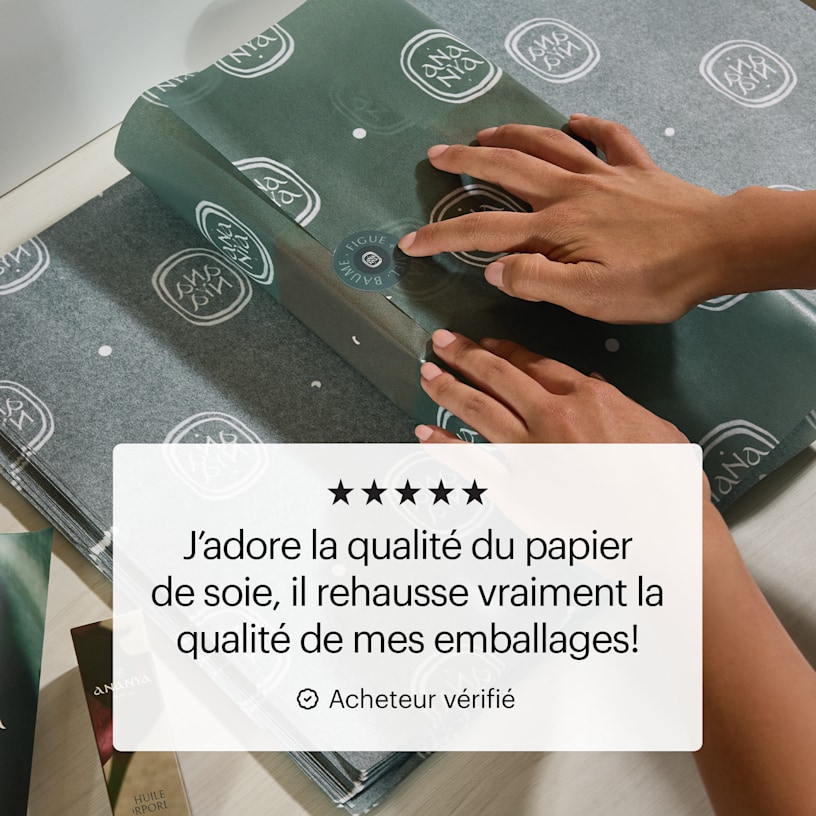 Deux mains en train d’envelopper une boîte cadeau de papier de soie avec impression personnalisée, et un avis client disant :
« J’adore la qualité du papier de soie. Ça améliore vraiment mes emballages! »