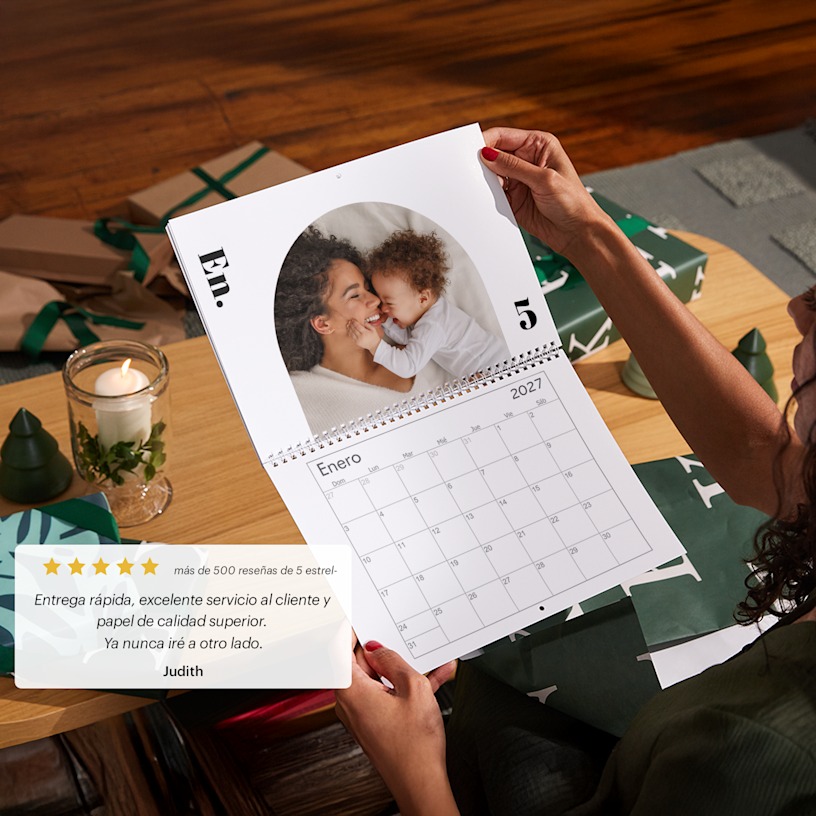 Una mujer sujetando un calendario de pared con foto, abierto y mostrando una foto de ella con su bebé. 