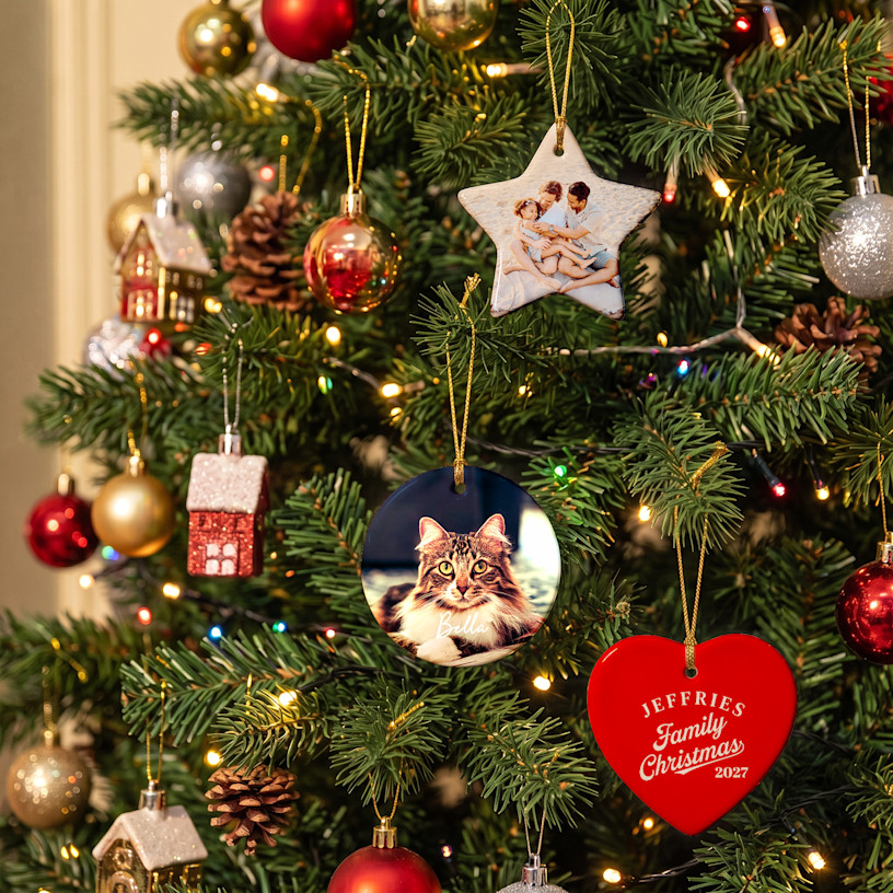 Two Christmas ornaments featuring a family photo and family name, hanging from a tree. An arrow points to the included golden string, which makes the ornaments ready to hang when they arrive.
