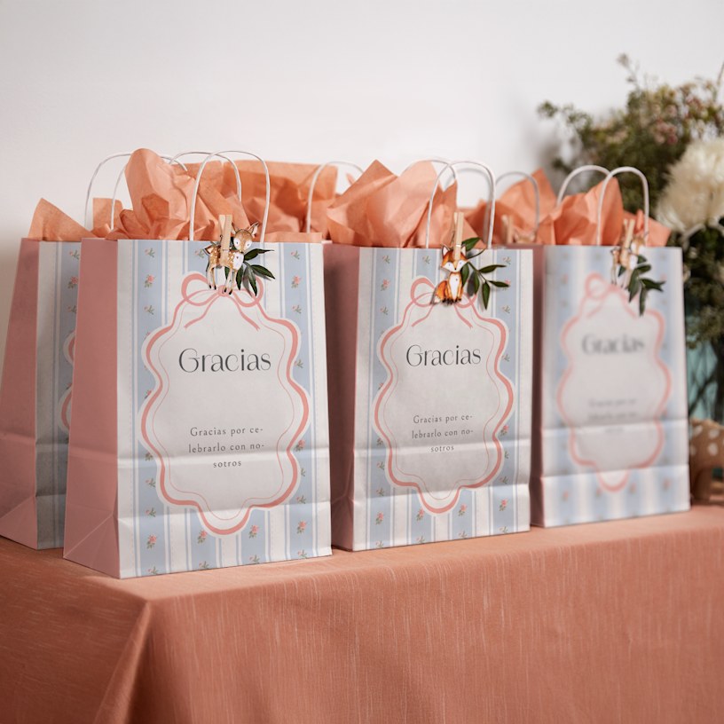 3 bolsas de regalo de la celebración de una boda en la que aparece un estampado floral y rellenas de papel de seda de color salmón.