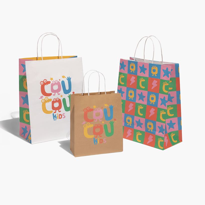 En hand som håller i två presentpåsar: en brun påse med fruktdesign för ett företag med namnet LUXA, och en större vit och gul påse som är märkt ”kids”.