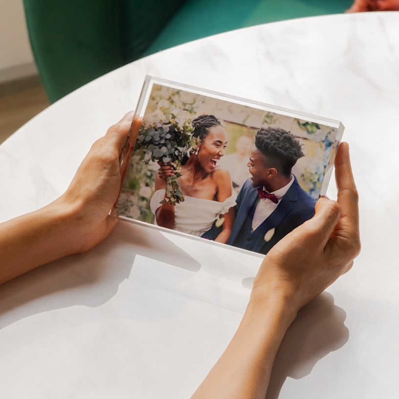 Manos sosteniendo un bloque de acrílico transparente con una foto que muestra el retrato de boda de una pareja recién casada.