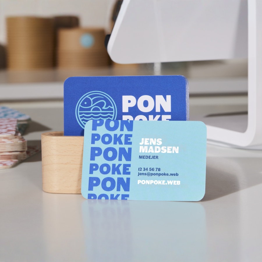 Et sæt blå og hvide visitkort med afrundede hjørner til en poke-restaurant, placeret på en disk.