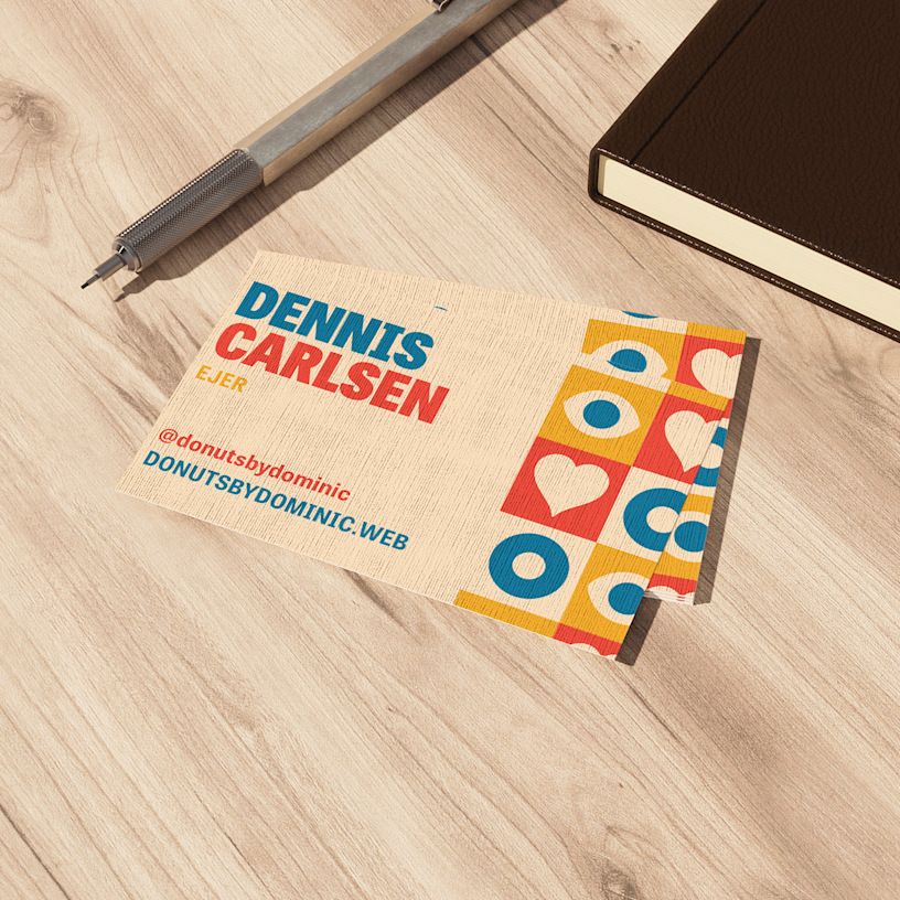 En stak visitkort i hør til en donutbutik ligger på en træbordplade ved siden af en notesbog og en kuglepen