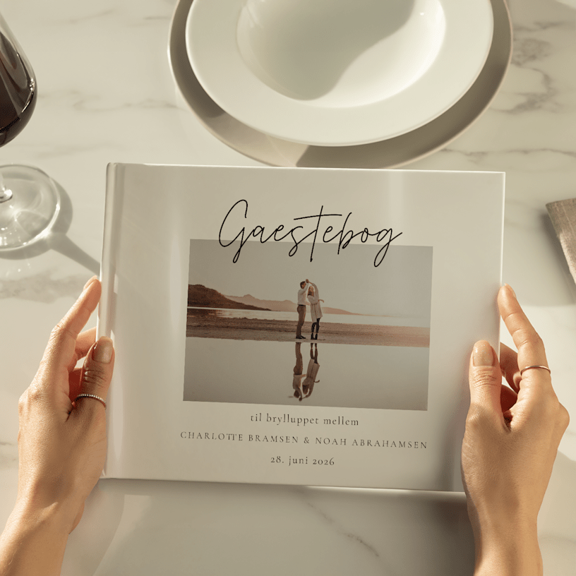 Hænder, der holder en gæstebog til et bryllup, der er tilpasset med et billede af parret på forsiden. 