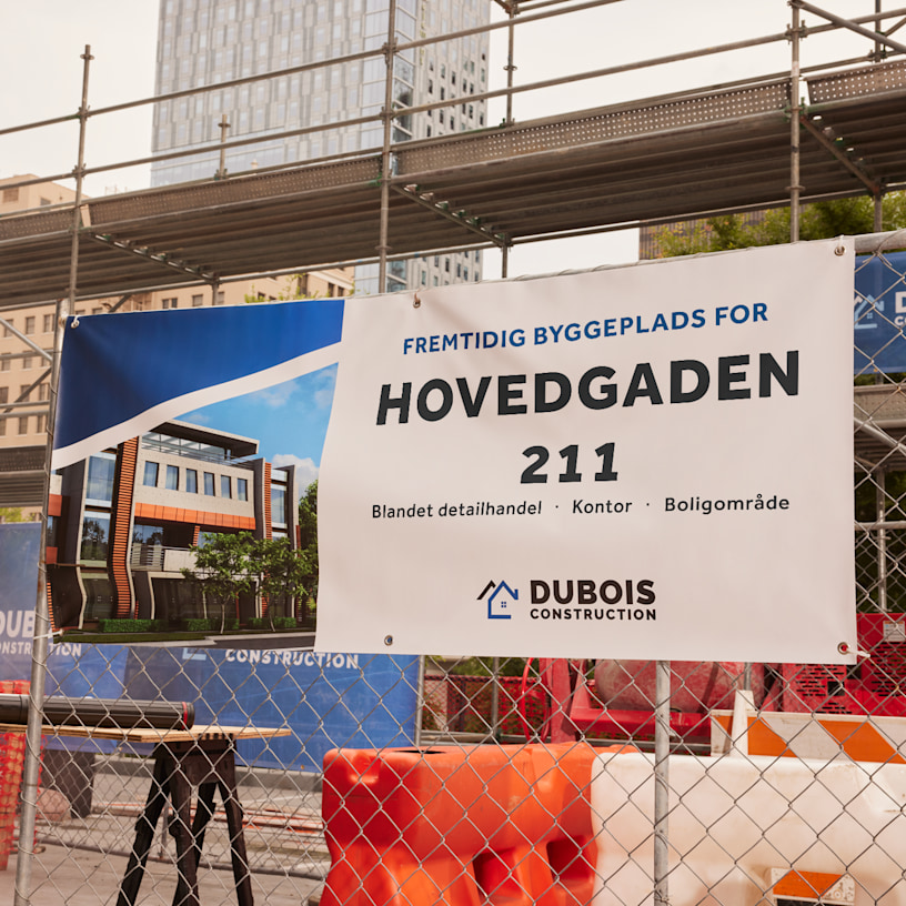 Et banner fra et byggefirma bundet til et hegn til en byggeplads med detaljer om den nye bygning.