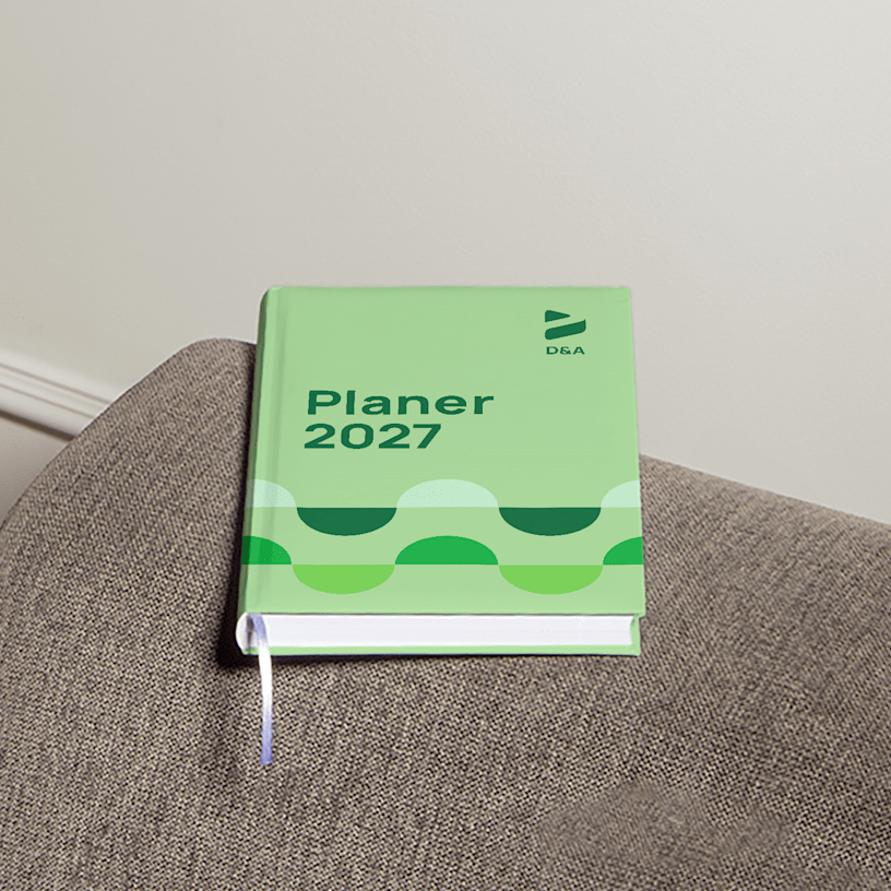 Ein Terminplaner mit Hardcover und Branding eines Designunternehmens liegt auf der Armlehne einer Couch.