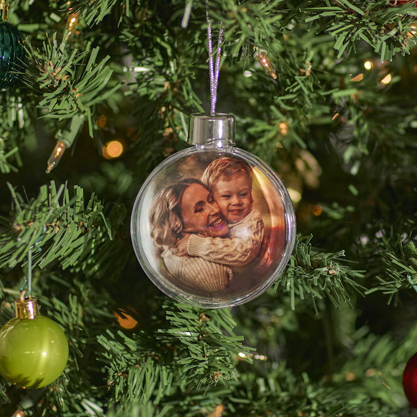 Ein Weihnachtsbaum mit einer personalisierten Christbaumkugel samt Foto einer Mutter, die ihren Sohn umarmt. 