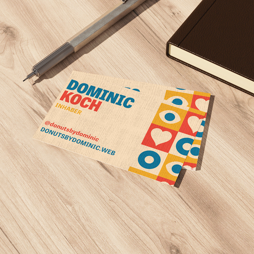 Ein Stapel Leinen-Visitenkarten für einen Donut-Laden liegt auf einer Theke neben einem Notizbuch und einem Kugelschreiber.