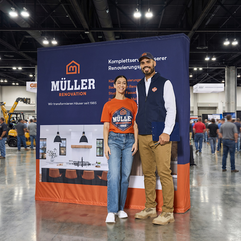 A man and a woman standing in front of a home renovation pop-up display at a tradeshow.