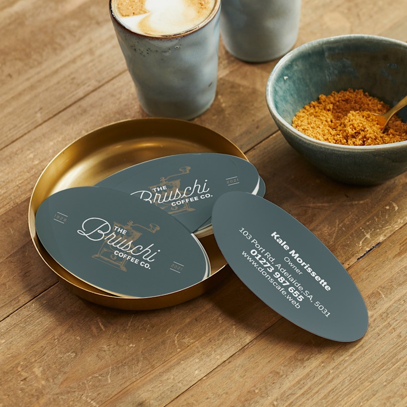 Oval business cards promoting a cafe with sophisticated typography, displayed on a table.