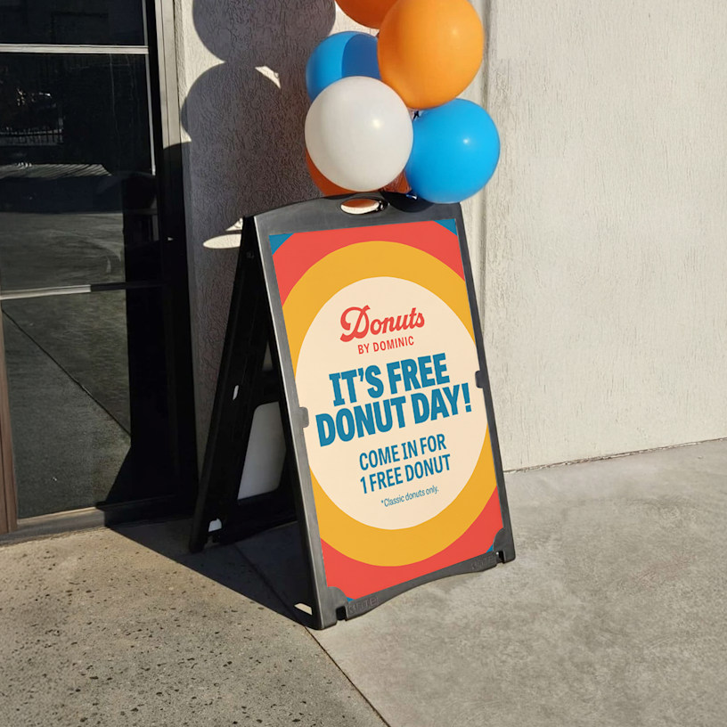 A black, water fillable A-frame promoting a Free Donut Day event, displayed outdoors.