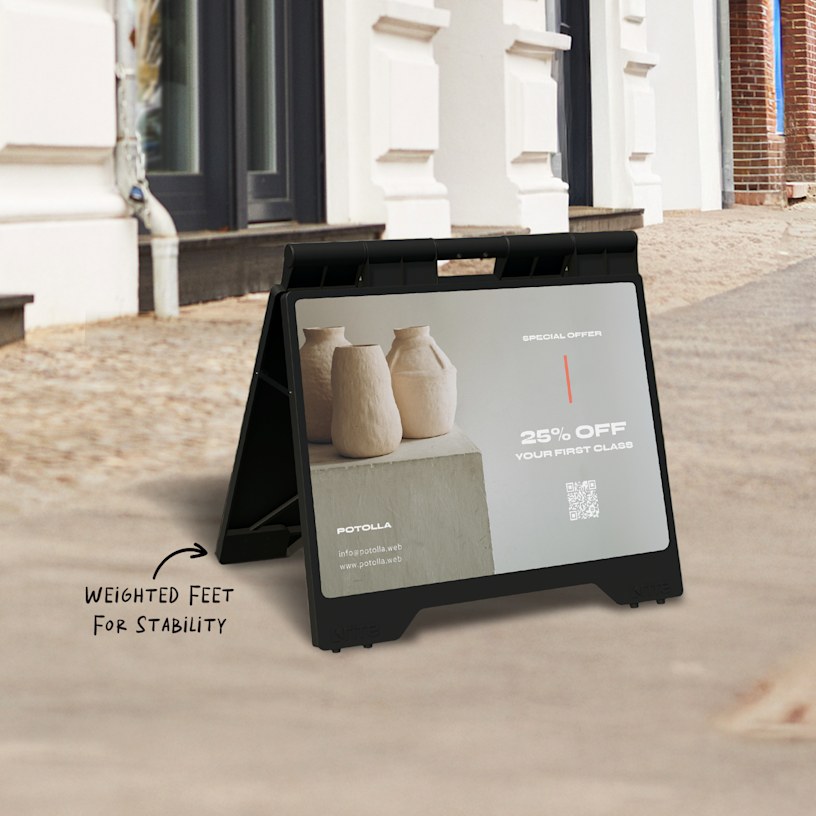 A black, small A-frame with a QR code for a pottery class, displayed outdoors.