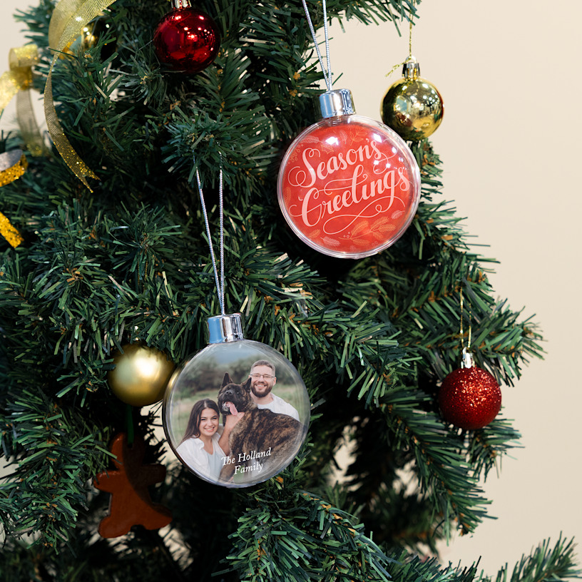 Two Christmas baubles hanging from a tree, with one featuring a typographic design and one featuring a family photo.
