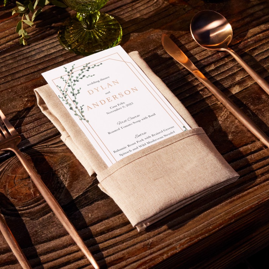A wedding menu with a modern design rests on a beige napkin on a wood table.