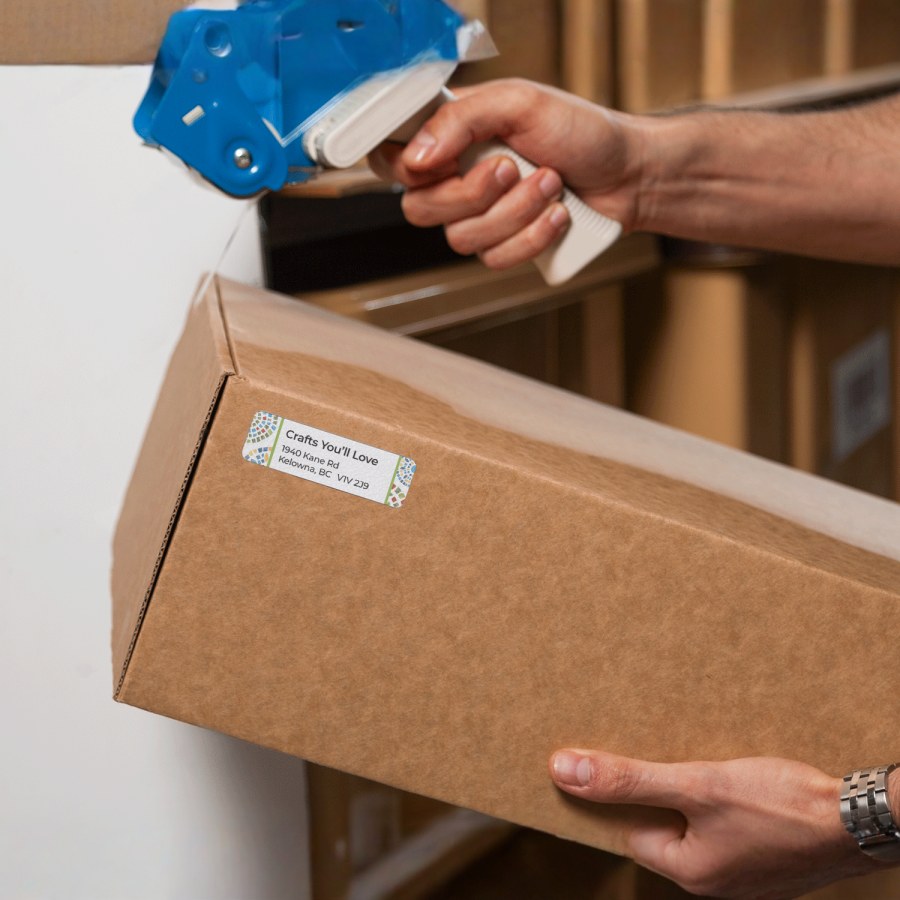 A person using a labeling machine to apply return address labels to a package.