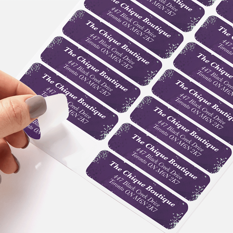 A person peeling a return address label for a boutique from a sheet of labels.