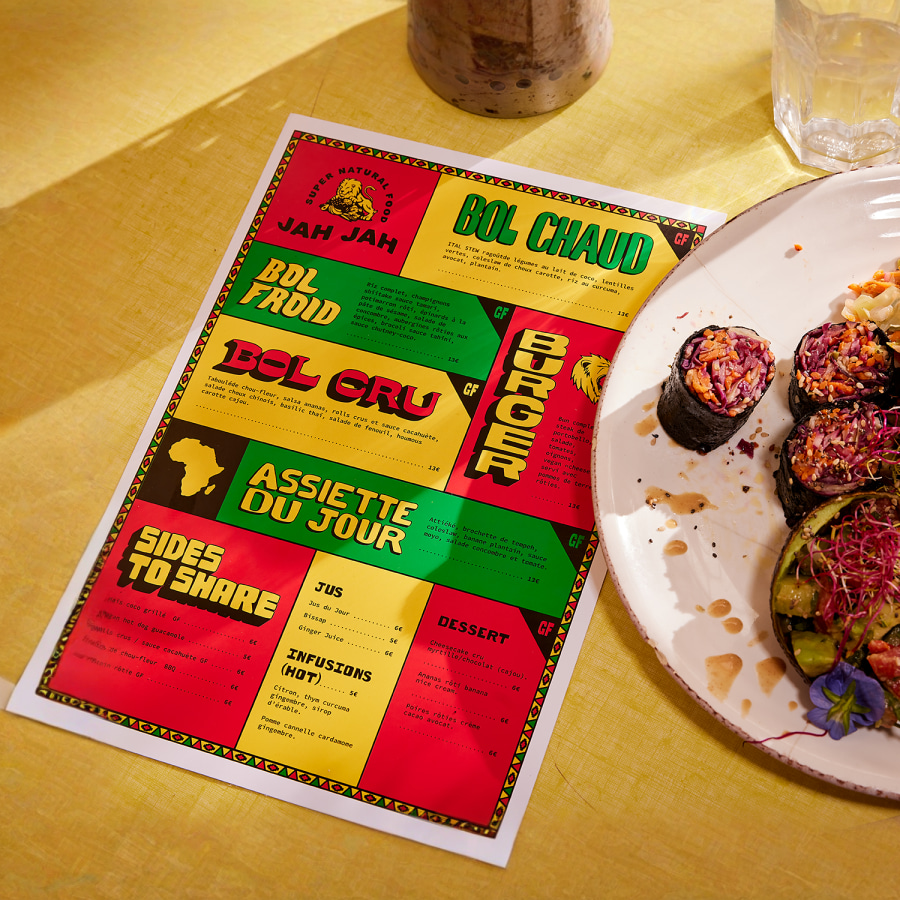 A colourful flat menu at a place setting in a restaurant, next to a dish of food. 