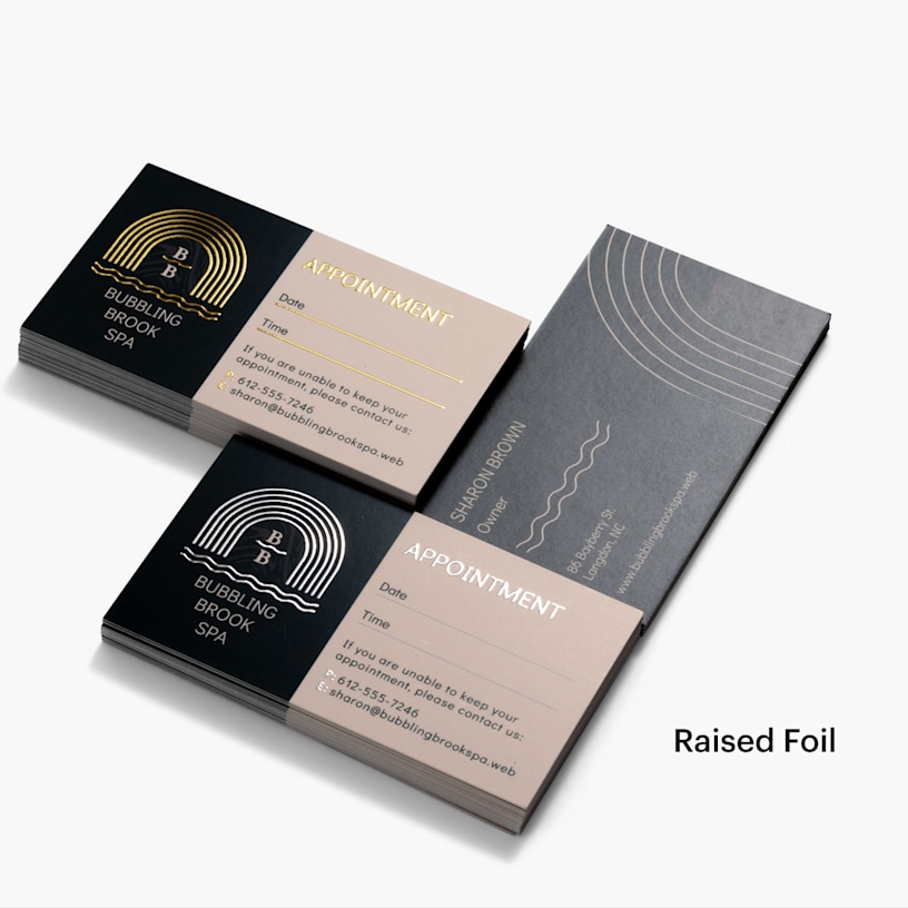 A stack of gold raised foil appointment cards and a stack of silver raised foil appointment cards, both for the same spa and using the same design.