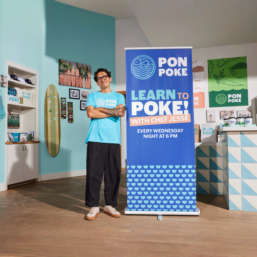 A man standing proudly next to his assembled poke bowl retractable banner.