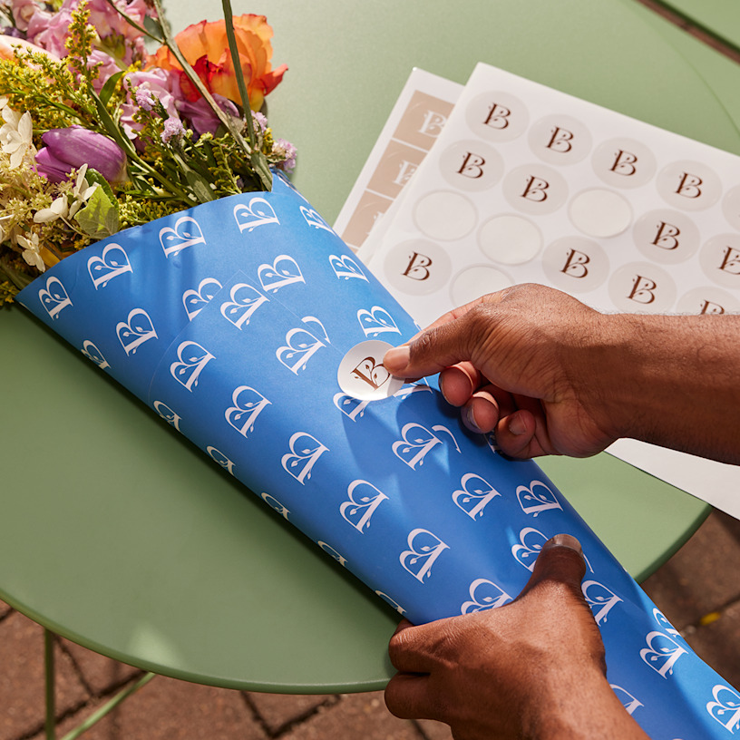 A person using a circle sticker from a sheet to seal a bouquet of flowers.