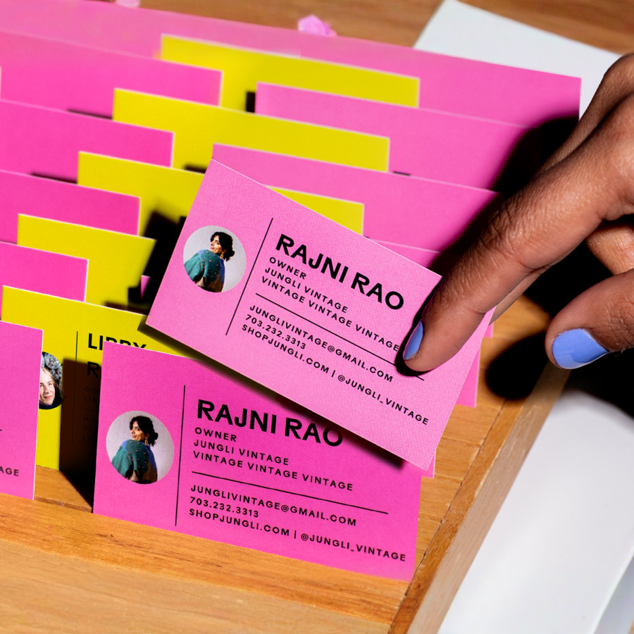 Pink and yellow business cards for a vintage shop in a wooden holder, with a hand pulling one out.