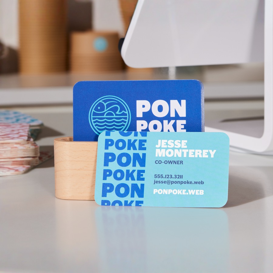 A set of blue and white rounded corner business cards for a poke restaurant, placed on a checkout counter.