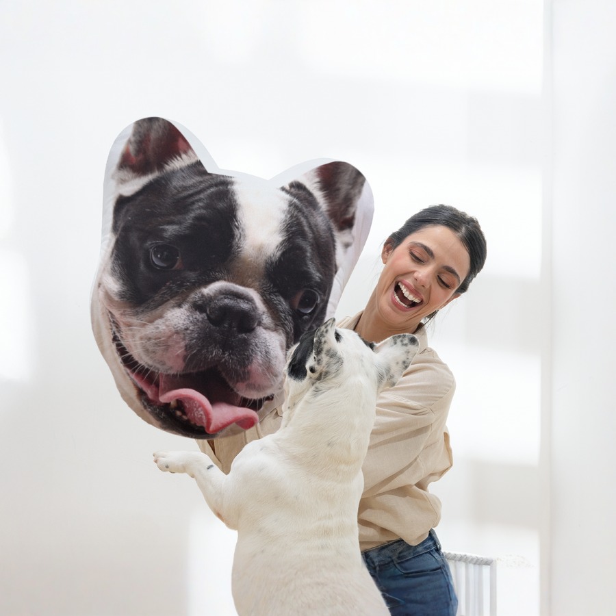 A woman showing her dog a pet face pillow featuring the dog’s face. 