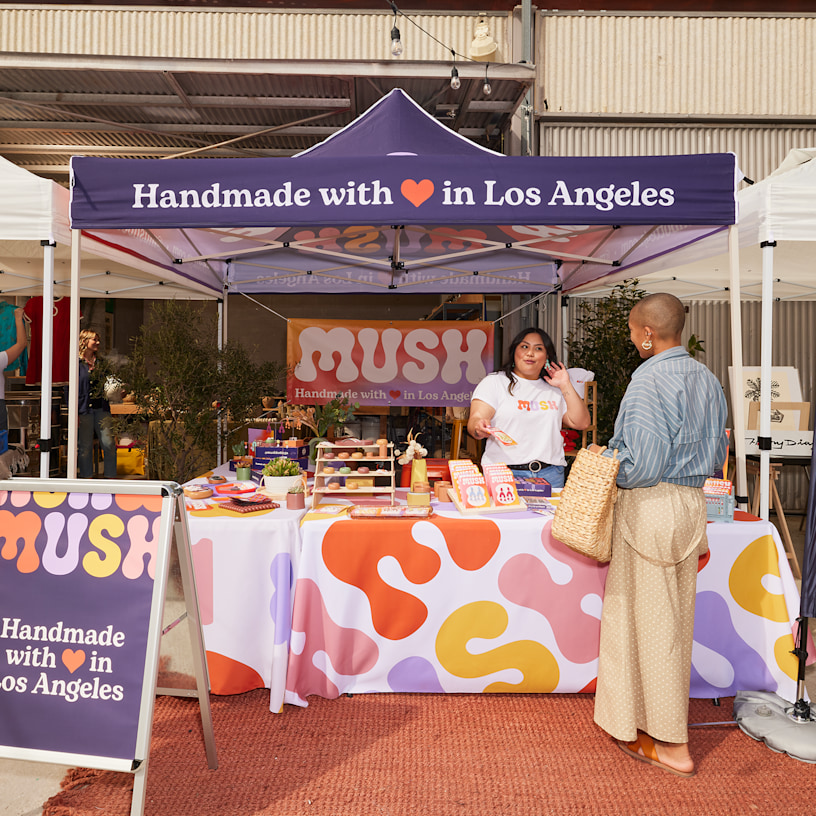 A handmade goods store set up underneath a canopy tent in an outdoor market.