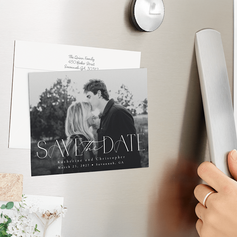 A save the date magnet displayed on the fridge, featuring a couple’s black and white engagement photo. 