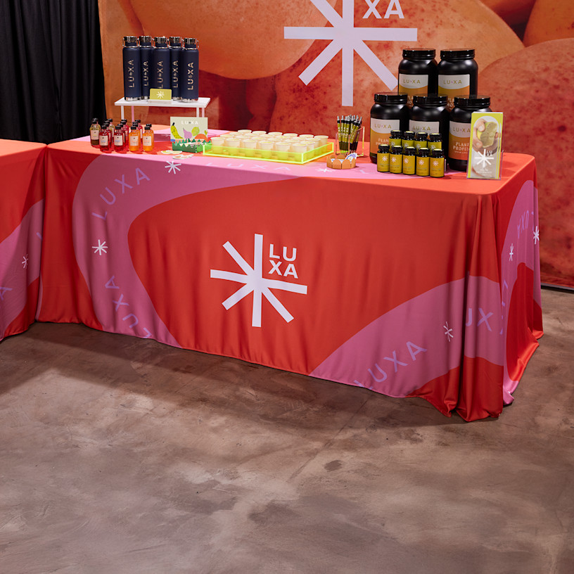 trade show table for a wellness brand with product samples, water bottles and custom branded rectangular tablecloth 