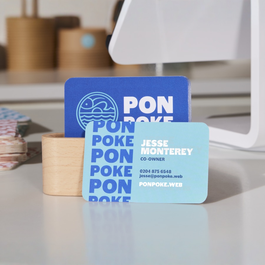 A set of blue and white rounded corner business cards for a poke restaurant, placed on a checkout counter.