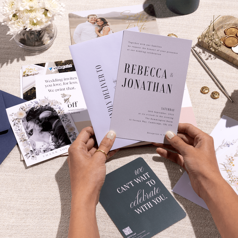 A pair of hands holding a wedding invitation printed with a bold font and a neutral colour palette. 